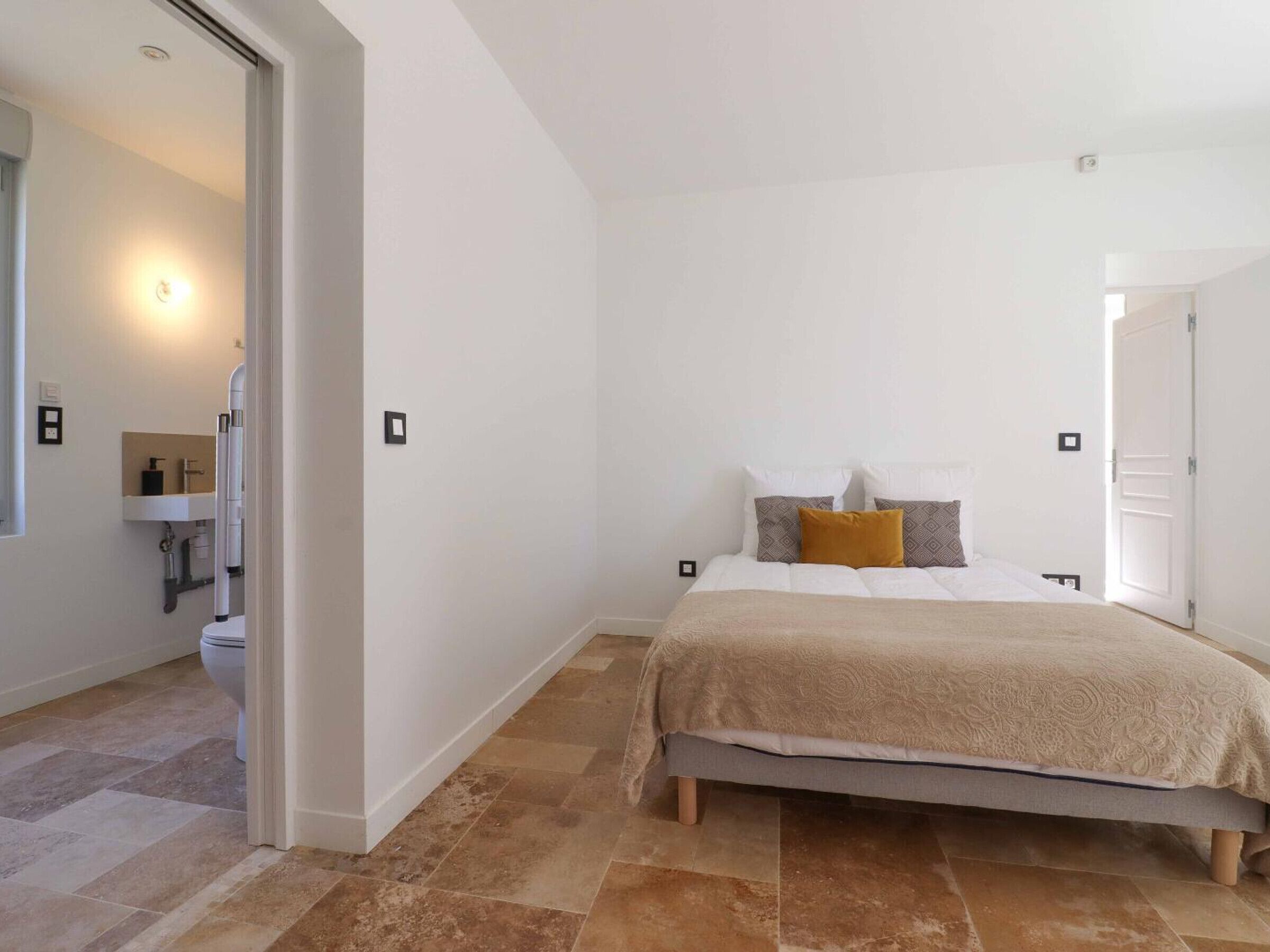 Een slaapkamer met een bed, een nachtkastje en een badkamer zichtbaar door een open deur.