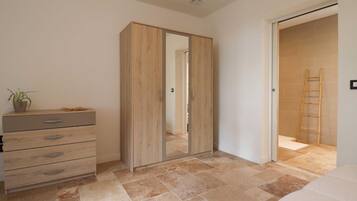 Une chambre à coucher avec une armoire, une table de chevet agrémentée d’une plante, un lit et une salle de bain avec une douche et une échelle.