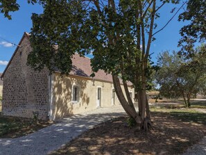 Un edificio de piedra con camino de grava y un árbol en primer plano.