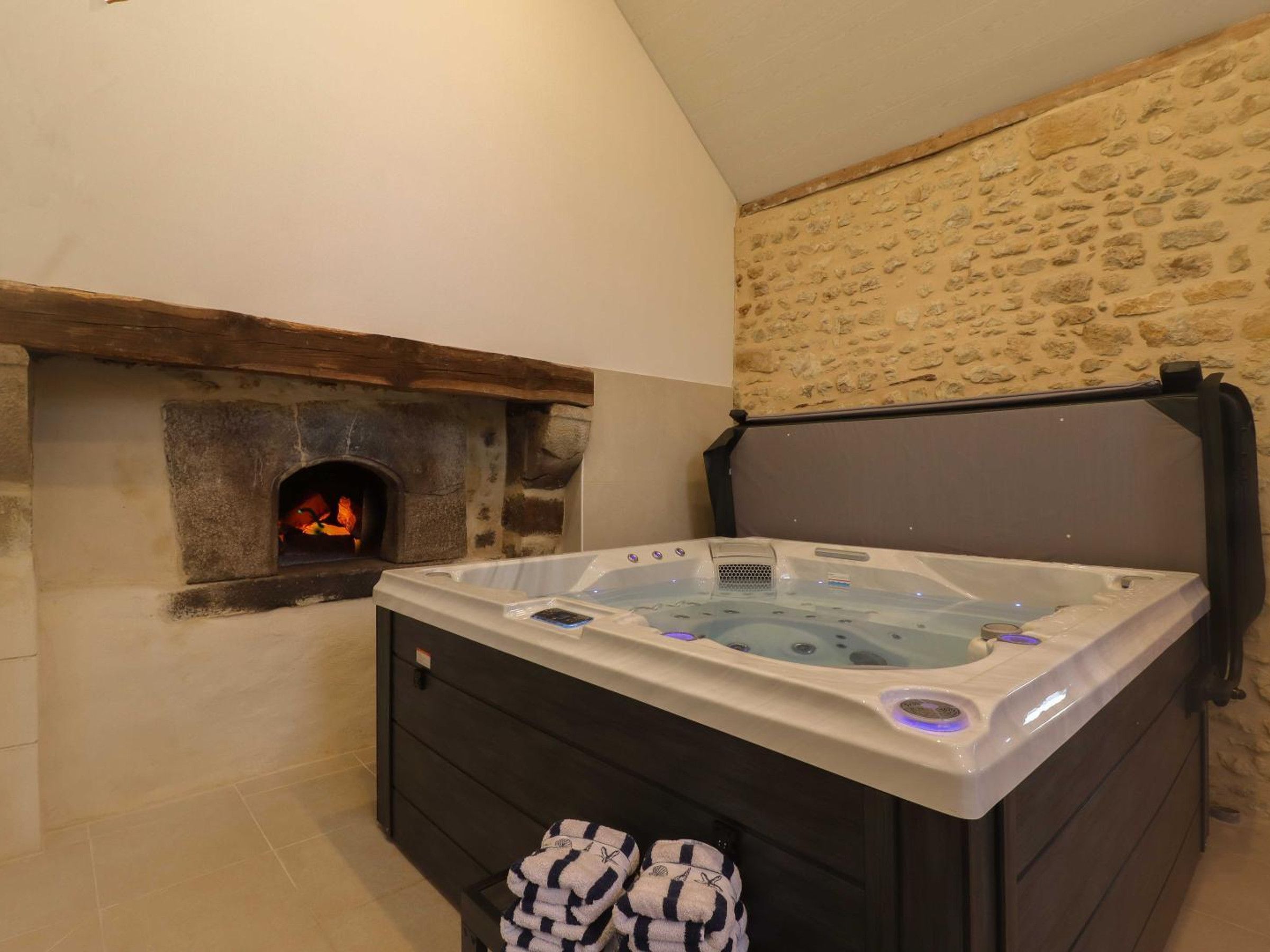 A hot tub with a stone wall and a fireplace in the background.