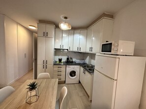 A compact kitchen with white cabinets, a washing machine, a microwave, and a dining area with a table and chairs. - Central Apartment with Terrace and Air Conditioning (Torremolinos)