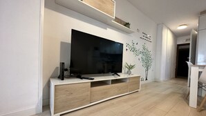 A modern living room with a flat-screen TV on a white console, wooden flooring, and a wall-mounted shelf with decorative items. - Central Apartment with Terrace and Air Conditioning (Torremolinos)