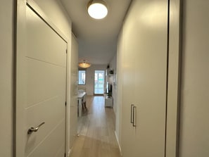 Ein Flur mit einer Tür links, ein Essbereich mit Tisch und Stühlen in der Mitte und eine Küchenzeile mit Schränken und einer Arbeitsplatte rechts.
