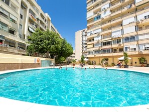 A swimming pool surrounded by multi-story residential buildings with balconies, trees, and outdoor seating areas. - Central Apartment with Terrace and Air Conditioning (Torremolinos)