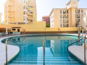 A swimming pool with a tiled edge, surrounded by a low wall, and adjacent to a multi-story building with balconies. - Central Apartment with Terrace and Air Conditioning (Torremolinos)