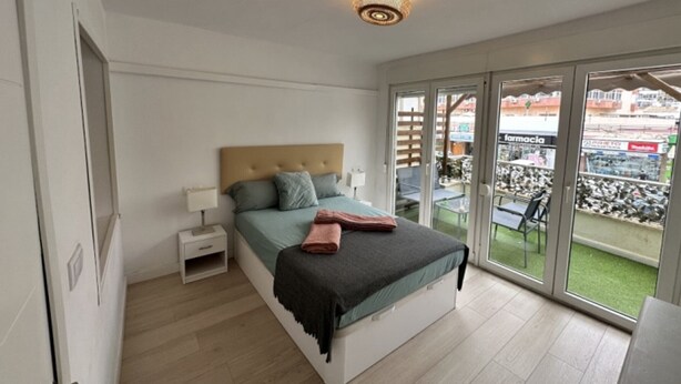 A bedroom with a bed, bedside table, and a view of a balcony with outdoor seating. - Central Apartment with Terrace and Air Conditioning (Torremolinos)