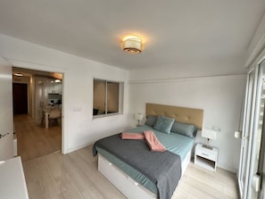 Ein Schlafzimmer mit Bett, Nachttischen, einem Fenster und einer Tür zu einem Badezimmer.