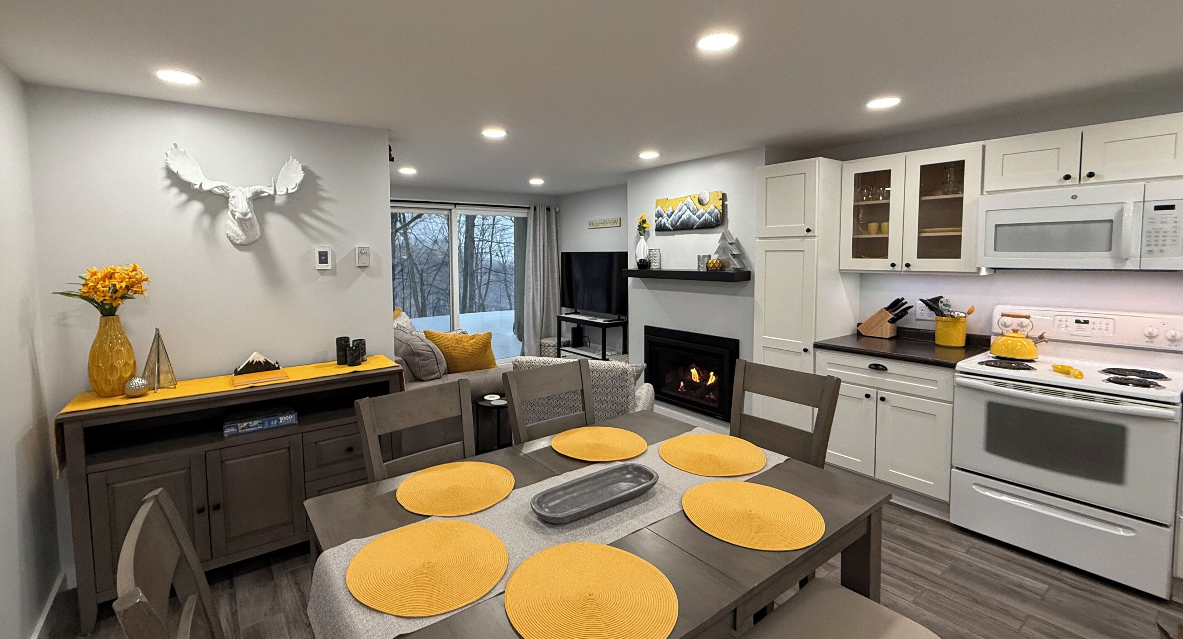 A modern kitchen with white cabinets, a microwave, and a stove. There is a dining table with yellow placemats and chairs.