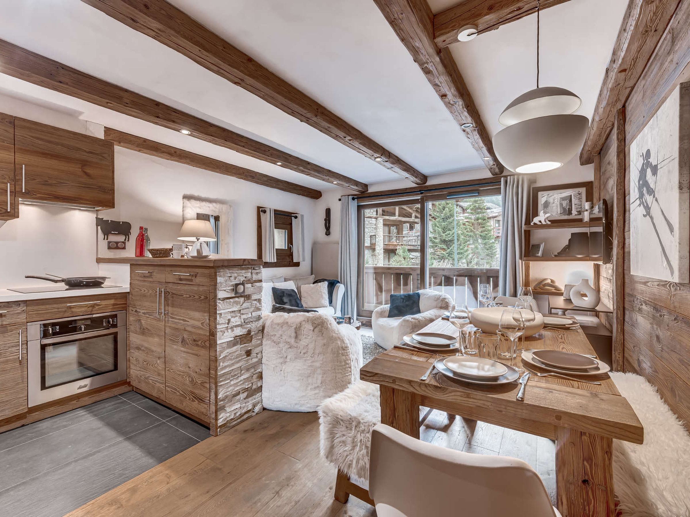 A modern kitchen with wooden beams, a dining area with a wooden table, and a view of a mountain landscape.