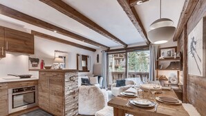 A modern kitchen with wooden beams, a dining area with a wooden table, and a view of a mountain landscape. - Apartment with parking - 6 guests (Val d'Isère)