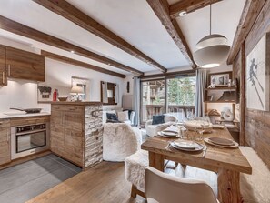 A modern kitchen with wooden beams, a dining area with a wooden table, and a view of a mountain landscape. - Apartment with parking - 6 guests (Val d'Isère)