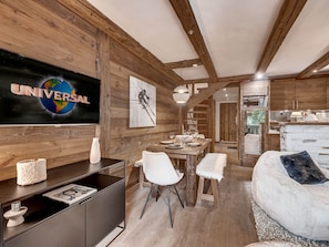 A modern interior with a wooden ceiling, a dining area, a sofa, and a television displaying 'UNIVERSAL'. - Apartment with parking - 6 guests (Val d'Isère)