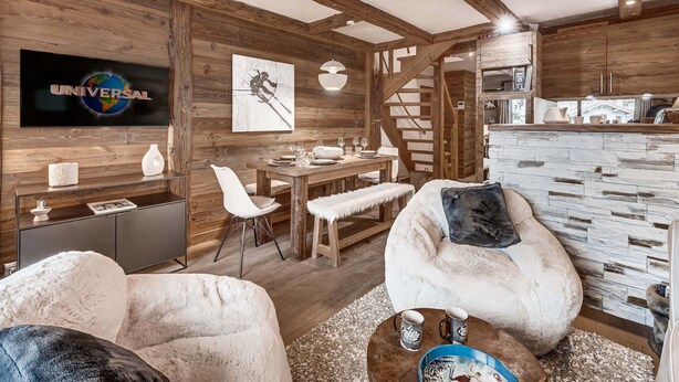 A cozy living room with a wooden ceiling, a television mounted on the wall, a dining area with a table and chairs, and a kitchen area with a stone backsplash. - Apartment with parking - 6 guests (Val d'Isère)