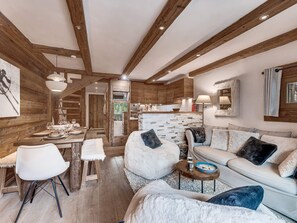 Ein modernes Interieur mit Holzboden, einer Essecke mit weißen Stühlen, einem Sofa mit flauschigen Kissen und einer Küche im Hintergrund.