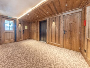 A spacious room with wooden paneling, a patterned carpet, and a large window. - Apartment with parking - 6 guests (Val d'Isère)