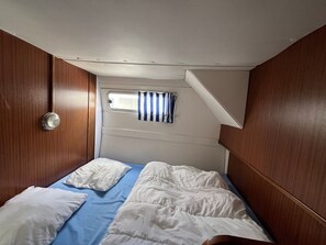 Una piccola stanza privata con un letto a castello, una finestra con tenda a righe e una porta con maniglia circolare.