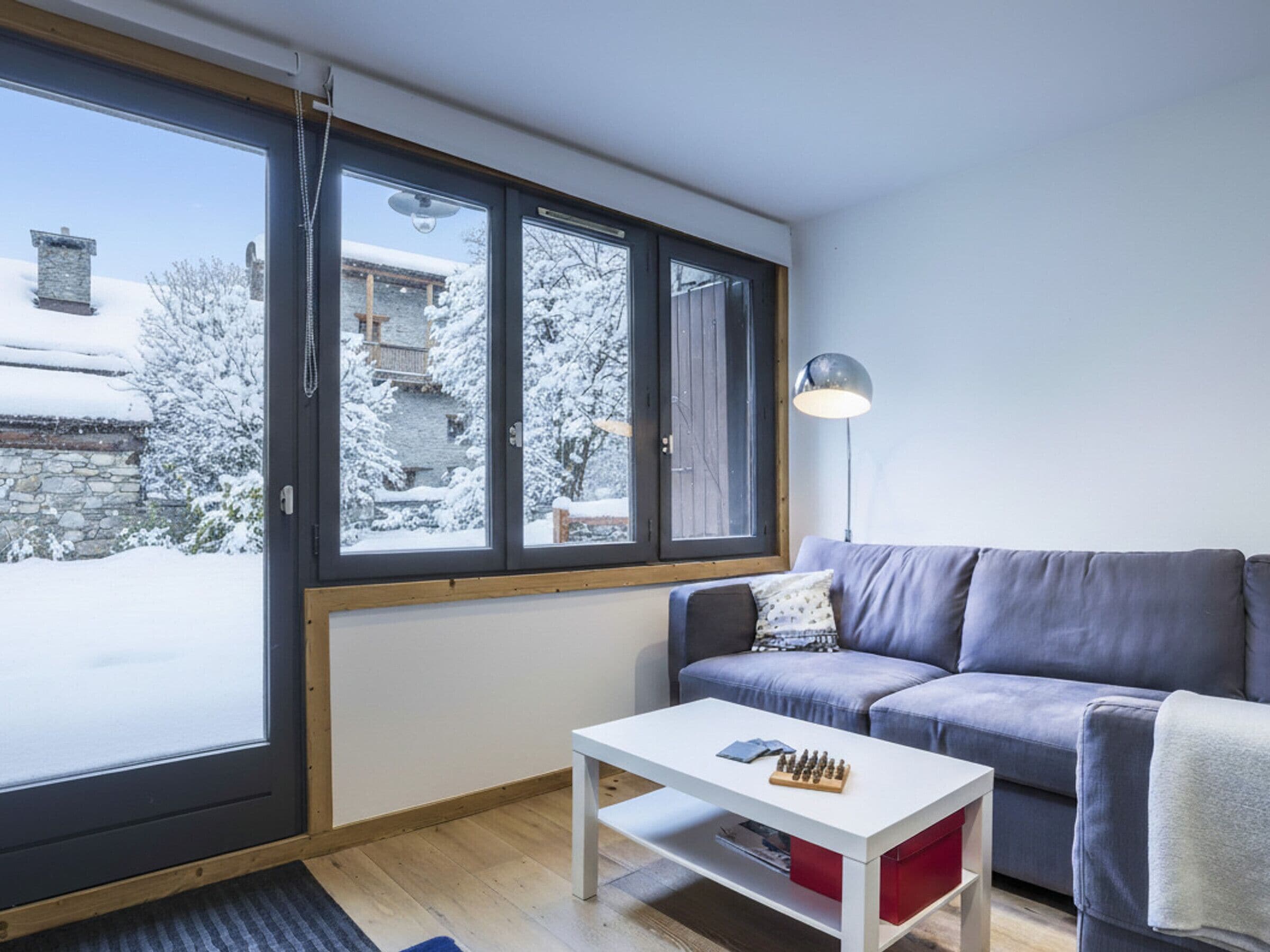 Ein modernes Wohnzimmer mit großem Fenster, einer Couch, einem Couchtisch und einer Lampe.
