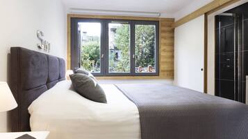 A modern bedroom with a large bed, a nightstand, a window with a view of greenery, and a wooden ceiling.