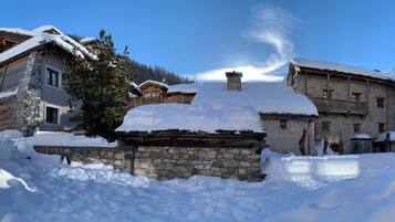 A snow-covered village with stone buildings, including a prominent stone house with a wooden roof.