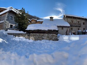 Un pueblo cubierto de nieve con edificios de piedra, incluyendo una casa de piedra destacada con tejado de madera.