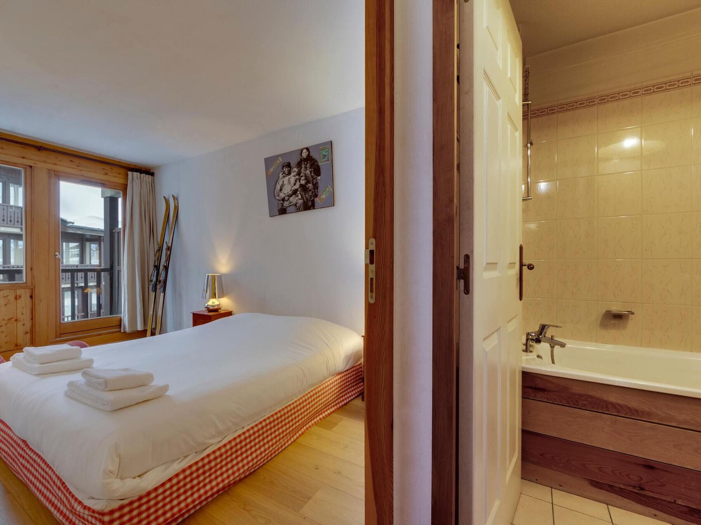 A hotel room with a large bed, a bathroom with a bathtub, and a window with curtains.