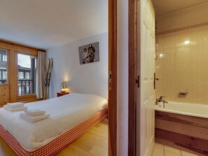 Habitación de hotel con una cama grande, un baño con bañera y una ventana con cortinas.