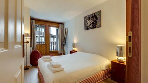 Ein Hotelzimmer mit einem großen Bett, einer Holztür, einem Fenster mit Vorhängen, einem Wandbild und einem Nachttisch mit Lampe.