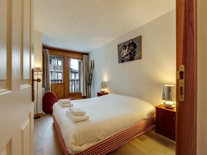 Ein Hotelzimmer mit einem großen Bett, einer Holztür, einem Fenster mit Vorhängen, einem Wandbild und einem Nachttisch mit Lampe.