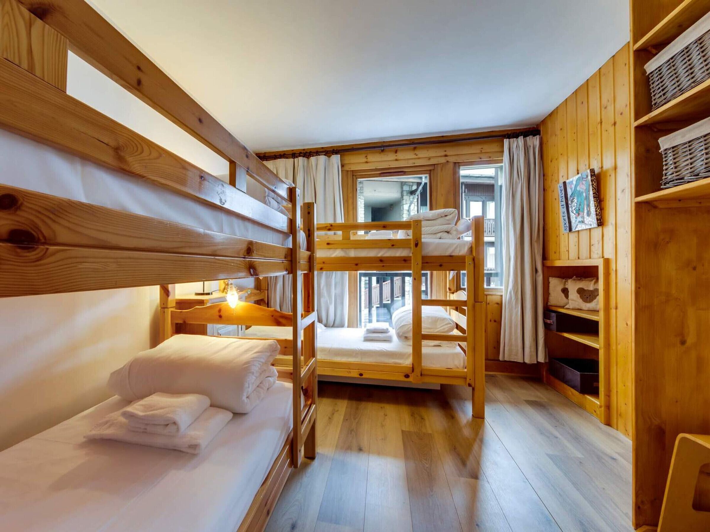 A bunk bed room with wooden walls, a wooden floor, and a window with curtains.