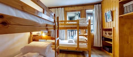 A bunk bed room with wooden walls, a wooden floor, and a window with curtains.