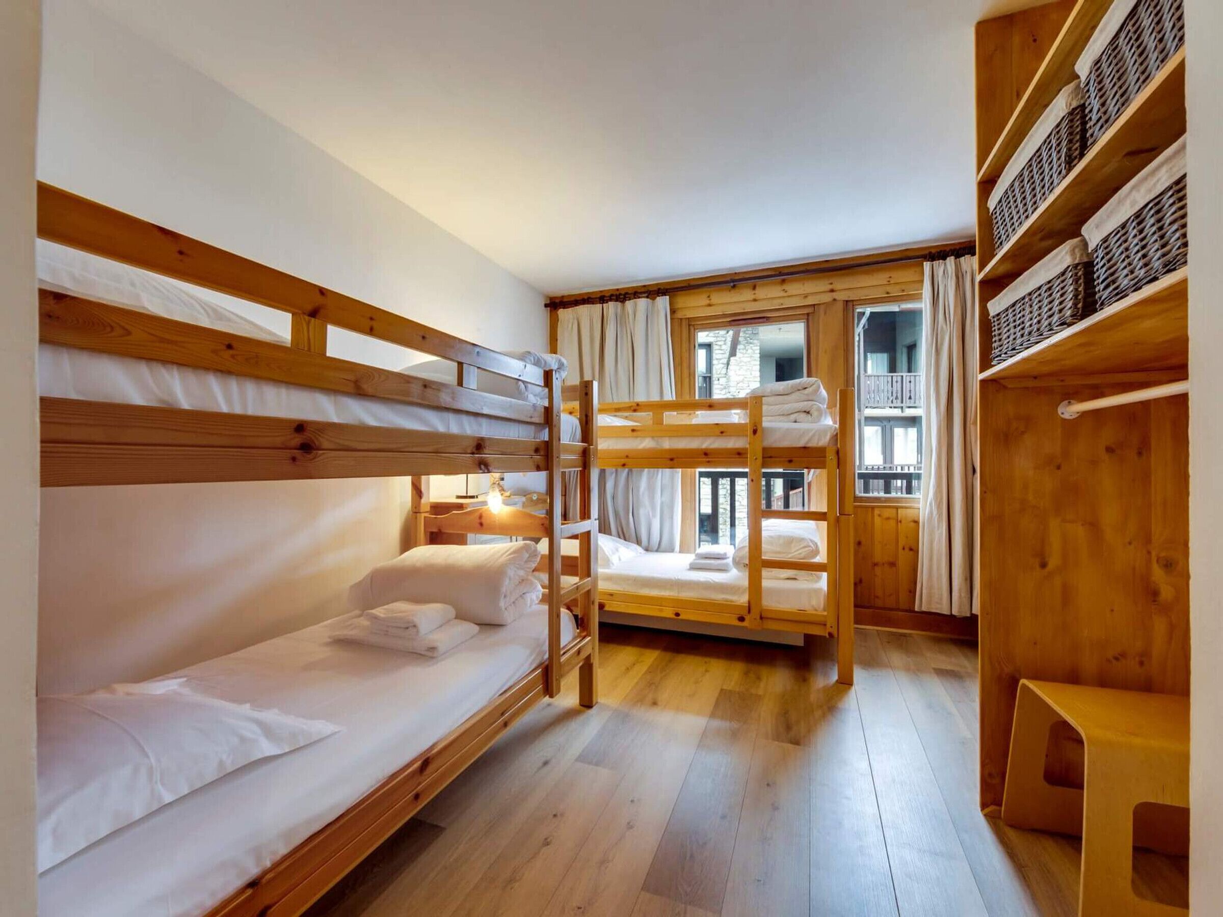 Un dormitorio con literas de madera, un banco de madera y una ventana con vista a un balcón.