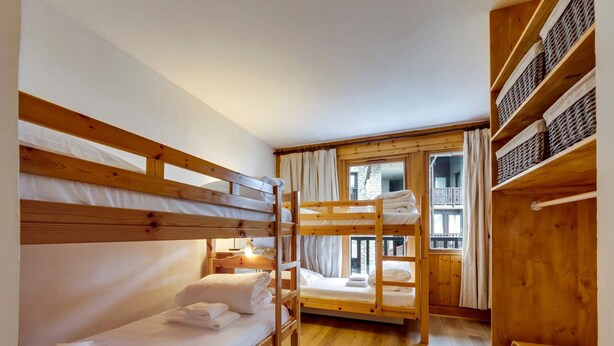 Ein Schlafraum mit Etagenbetten aus Holz, einer Holzbank und einem Fenster mit Balkonblick.