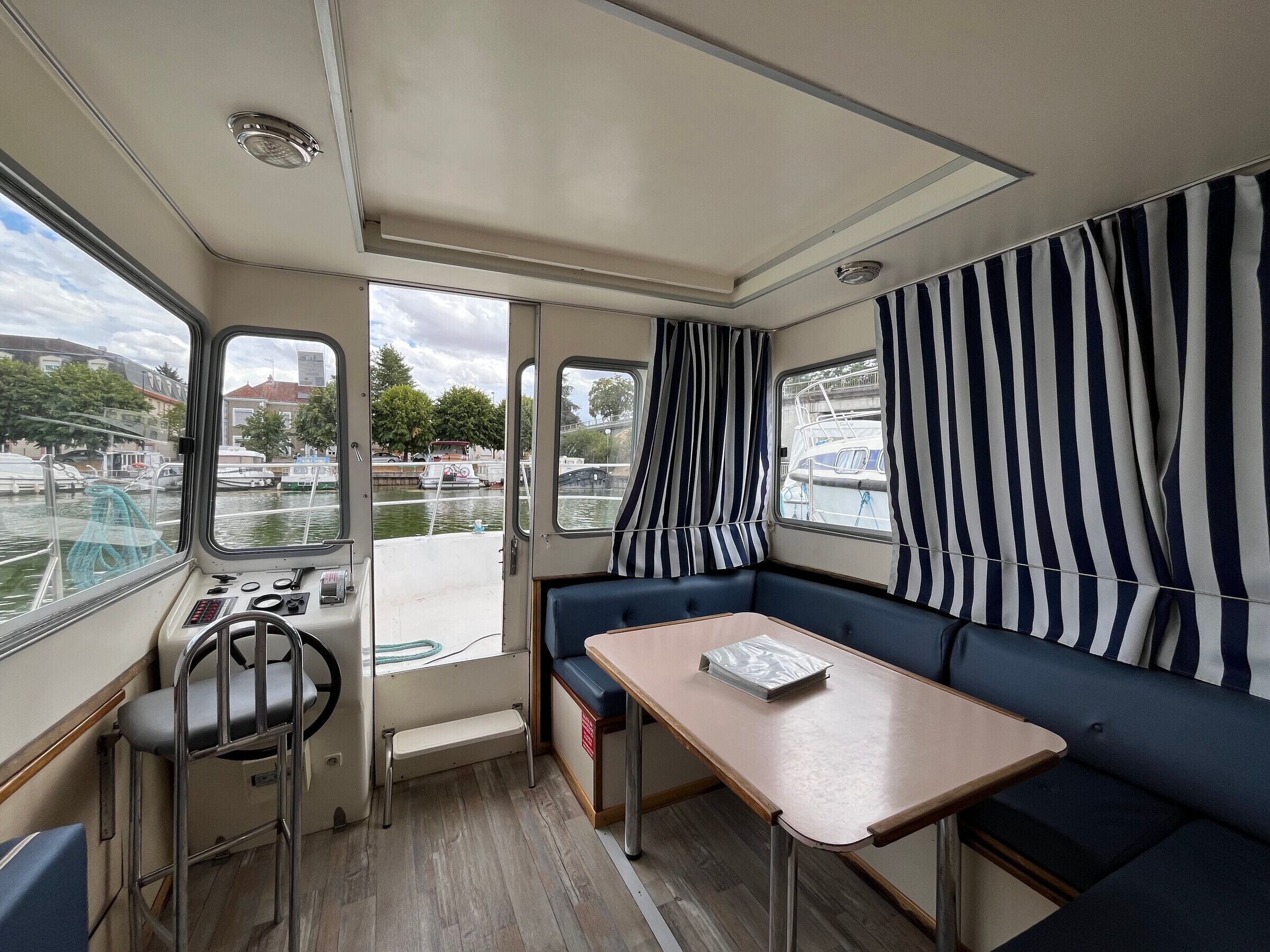 A cabin with a control panel, seating area, and windows offering views of the water.