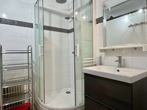 Ett modernt badrum med en dusch som är avskärmad med glasväggar, en vit tvättställ med en spegel ovanför och en kromad handdukshängare.