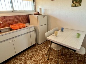 Ett kompakt kök med kylskåp, diskho och ett matbord med stolar.