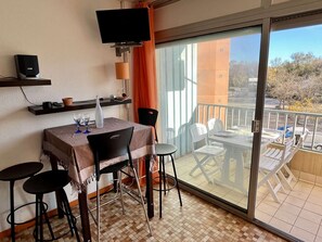 Un balcon avec une table et des chaises, un téléviseur fixé au mur et une vue sur l’extérieur.