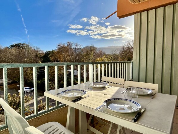 Un espace de restauration en plein air avec une table dressée pour deux personnes, offrant une vue panoramique sur un paysage pittoresque, avec des arbres et des montagnes.