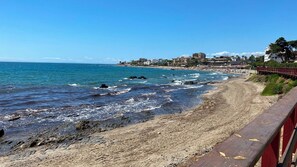 A coastal beach with a rocky shoreline, a wooden walkway, and buildings in the background. - Apartment Next to Max Beach | Ocean, year-round swimming pools, and parking (AN)