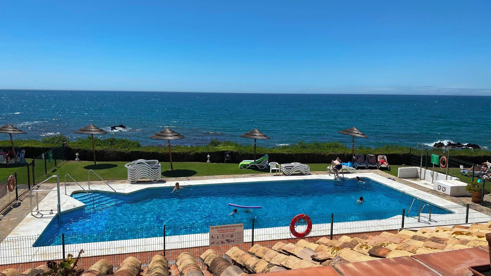 Ein Pool mit Meerblick, umgeben von Liegestühlen und Sonnenschirmen.