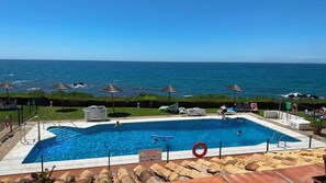 A swimming pool with a view of the ocean, surrounded by lounge chairs and umbrellas. - Apartment Next to Max Beach | Ocean, year-round swimming pools, and parking (AN)