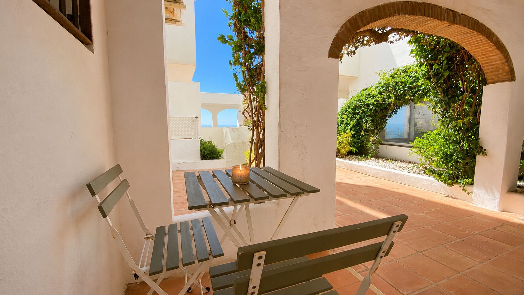 An outdoor patio with a table and benches, surrounded by white walls and a tiled floor.