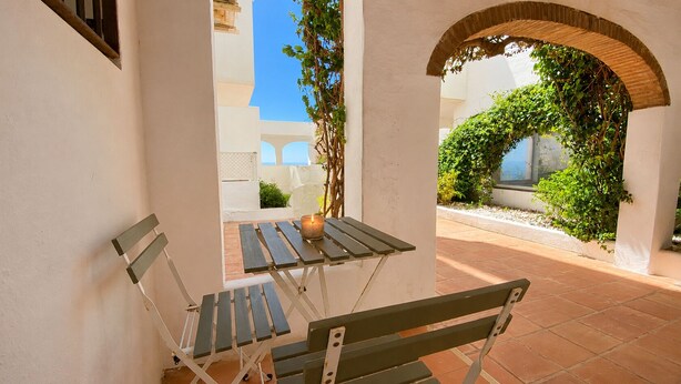An outdoor patio with a table and benches, surrounded by white walls and a tiled floor. - Beach Getaway with a Pool and Parking (AN)