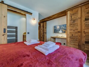 A room with a large bed, wooden beams, a wall-mounted light, a painting, and a desk with a lamp. - Cozy apartment near slopes - 6 guests (Val-d'Isère)