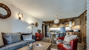 Ein modernes Wohnzimmer mit Sofa, Sessel, Couchtisch und einer Küche im Hintergrund.