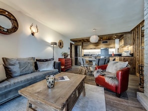 A modern living room with a sofa, armchair, coffee table, and a kitchen in the background. - Cozy apartment near slopes - 6 guests (Val-d'Isère)