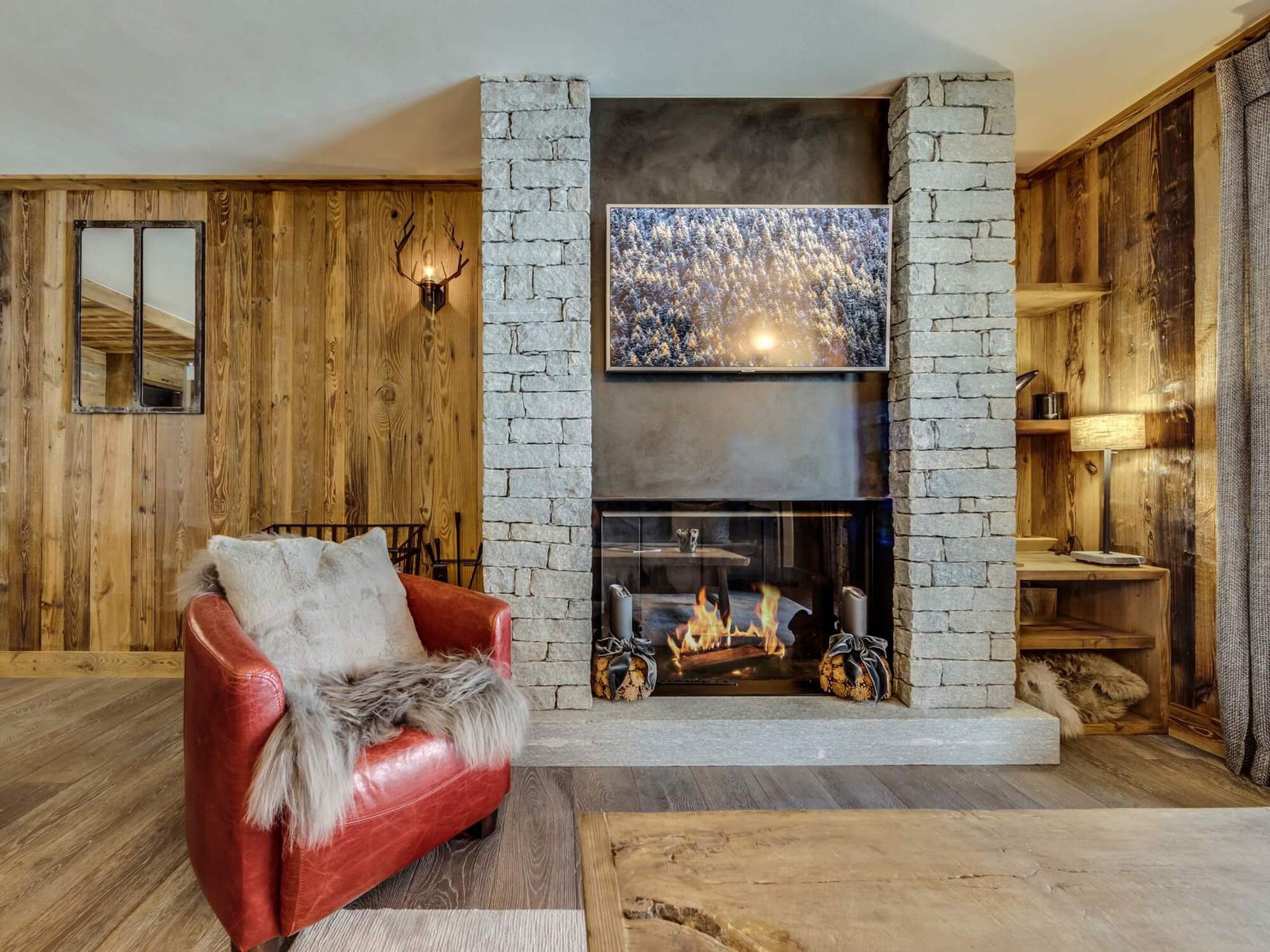 A cozy living room with a stone fireplace, a red leather sofa, and wooden walls.