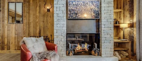 A cozy living room with a stone fireplace, a red leather sofa, and wooden walls.