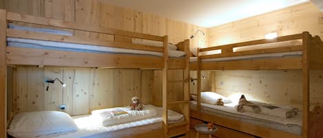 Habitación con literas, paredes de madera y un taburete pequeño.