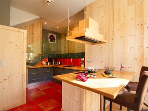 Eine moderne Küche mit Holzschränken, einer roten Spritzschutzwand und einem Essbereich mit einem Holztisch und -stühlen.