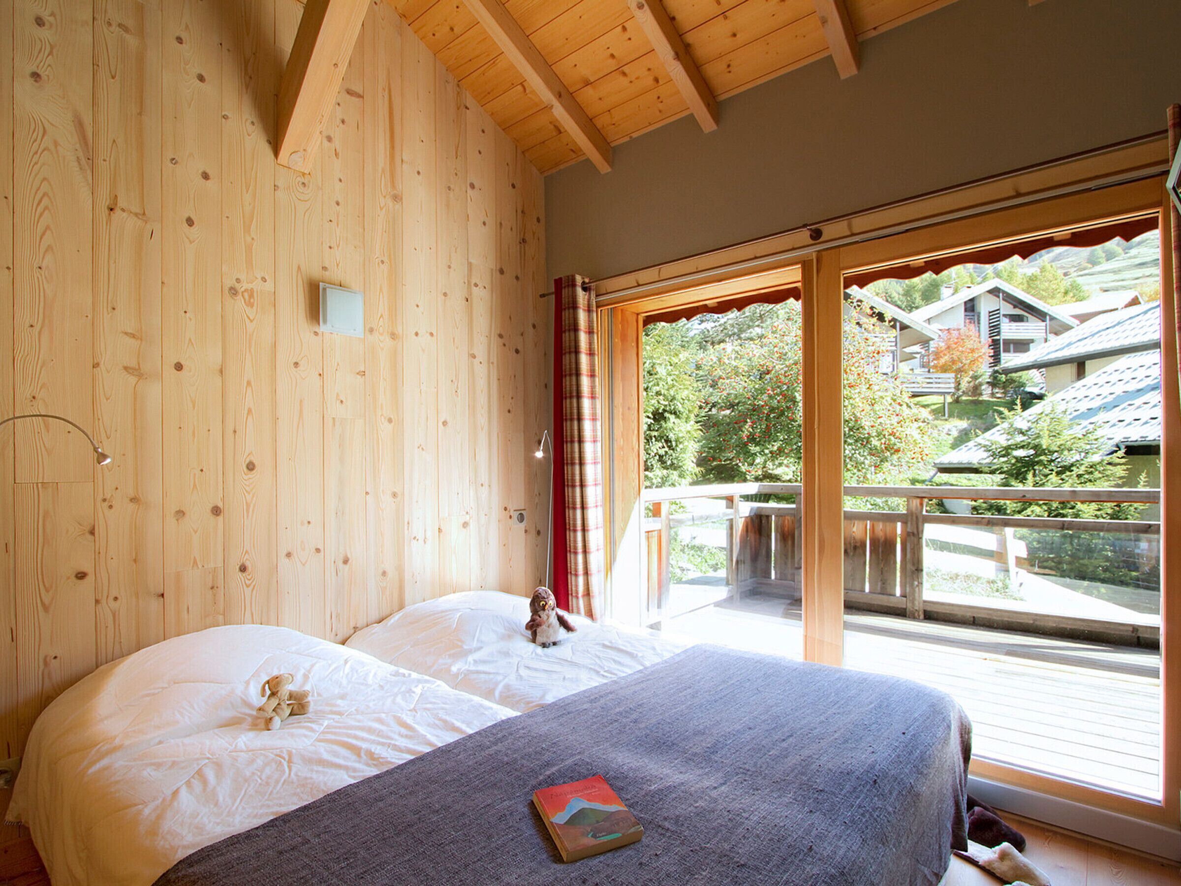Quarto com duas camas, janela com vista para casas e teto de madeira.